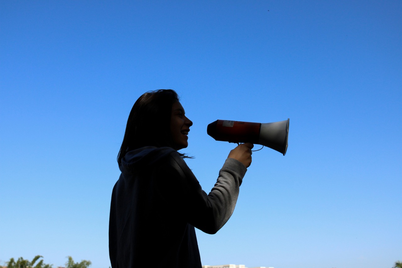 Woman speaking into a megaphone against a blue sky